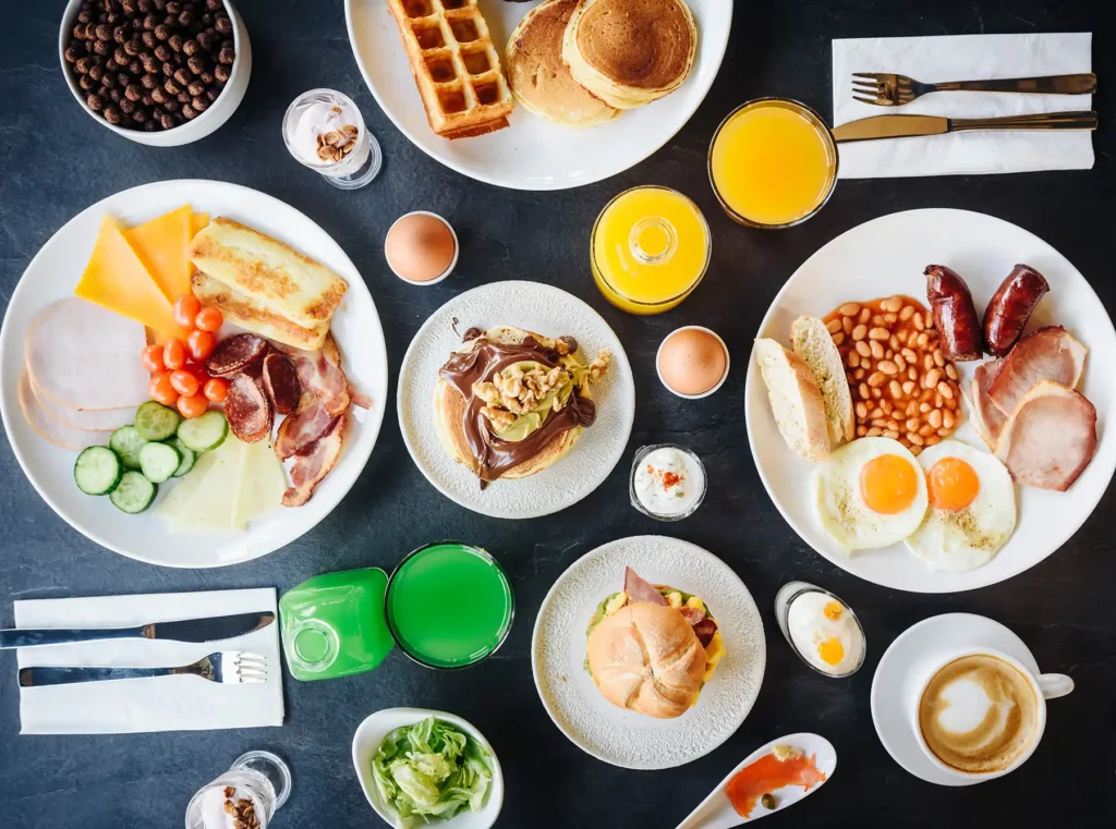 Top view of breakfast plates with pancakes, eggs, cold cuts, and fresh juice at Bread and Spread