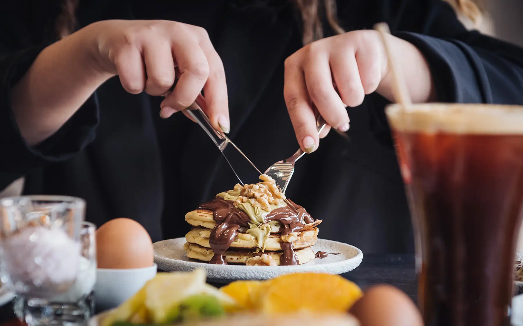 Person cutting fluffy pancakes with chocolate and nuts at Bread and Spread