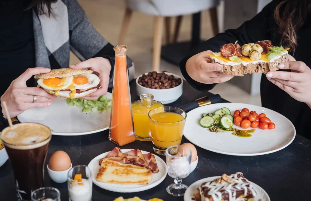 Two people holding DIY breakfast creations with eggs, meats and veggies at Bread and Spread
